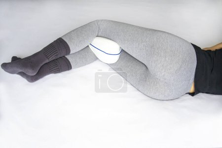 Foto de Chica delgada se encuentra de lado en la cama con una almohada ortopédica para las rodillas entre las piernas - Imagen libre de derechos