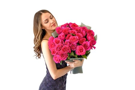 Young woman in black dress, holding bouquet of pink roses smiling and looking away on isolated white background, studio shot.