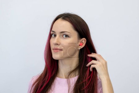 Téléchargez les photos : Beautiful young woman with bright pink hair in a pink T-shirt shows her ear with earplugs. Portrait of a woman looking into the camera - en image libre de droit