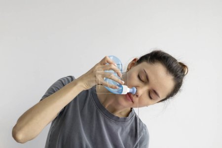 Girl rinses her nose with saline solution at home Using Neti Pot. Treatment and prevention of colds. How to rinse your nose when you have a runny nose