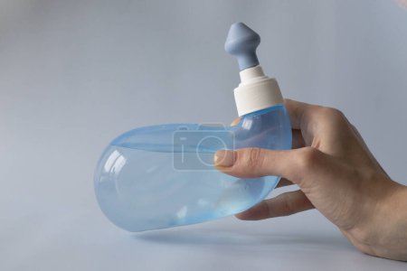 Neti Pot. Ayurvedic medical tools for cleaning your nose with water and salt at home. Blue bowl of water in a womans hand.