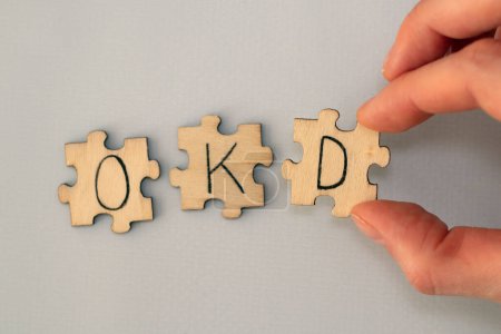 Photo for Obsessive compulsive disorder. Text lettering OCD handwritten on wooden puzzles. A womans hand assembles the puzzle - Royalty Free Image