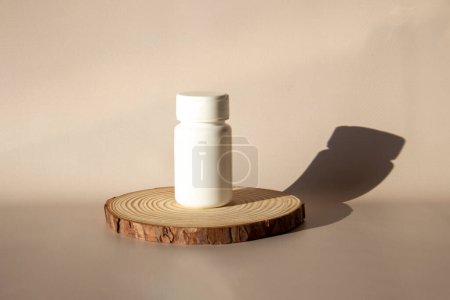 Foto de Burla de una píldora blanca y suplemento tarro en un podio de madera sobre un fondo beige en el sol - Imagen libre de derechos