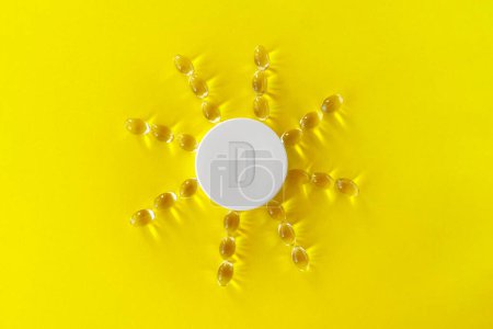 Gelber Hintergrund mit gelben Medikamentenkapselpillen auf gelbem Hintergrund in Form der Sonne mit Strahlen, die aus dem Deckel kommen und Vitamin D anzeigen..
