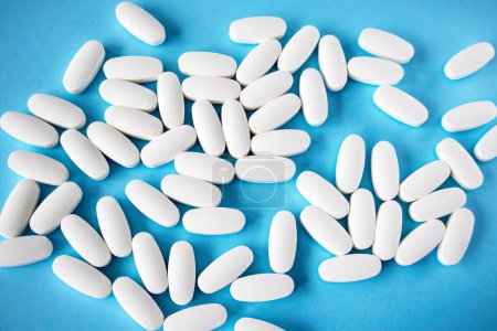 Photo for L glutamine white oval tablets scattered on a blue background, view from above. - Royalty Free Image