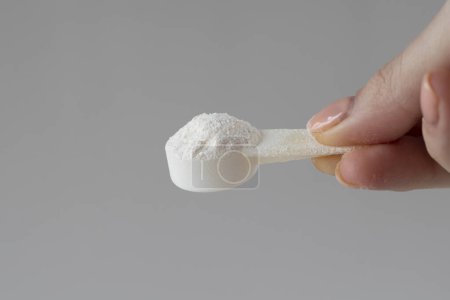 A measuring spoon with electrolyte powder and sports nutrition on a gray background in a womans hand.