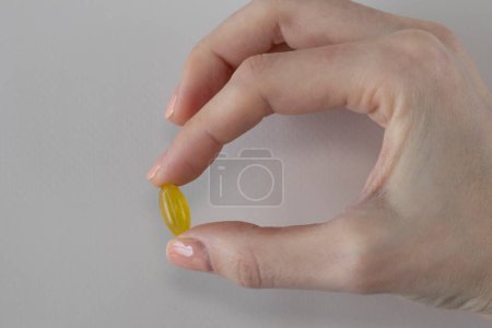 Foto de Cápsula amarilla de suplemento de aceite de orégano en una mano de mujer. - Imagen libre de derechos