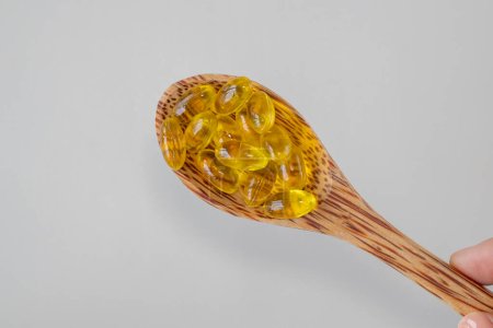 Téléchargez les photos : Wooden spoon with yellow capsules of oregano oil supplement. Natural antibiotic. - en image libre de droit