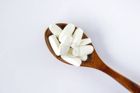 Foto de L glutamine white oval tabletsin a wooden spoon on a white background, top view - Imagen libre de derechos