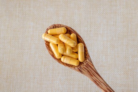 Photo for Coenzyme Q10 vitamin capsules in a wooden spoon on a beige background. Top view, copy space. Close-up - Royalty Free Image