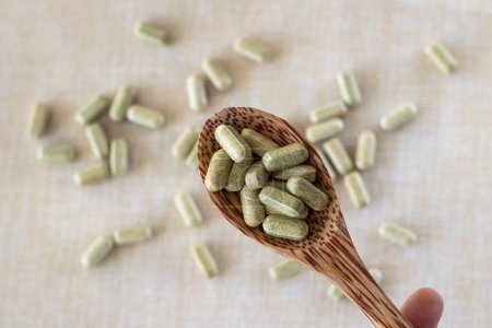 Vitamin aus Brokkoli-Sulforaphan in Kapseln in einem Holzlöffel auf beigem Hintergrund. Tabletten und Medikamente in grün.