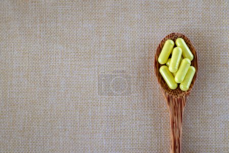 Foto de Cápsulas amarillas Quercetina en una cuchara de madera sobre un fondo beige. Vista superior, espacio de copia - Imagen libre de derechos