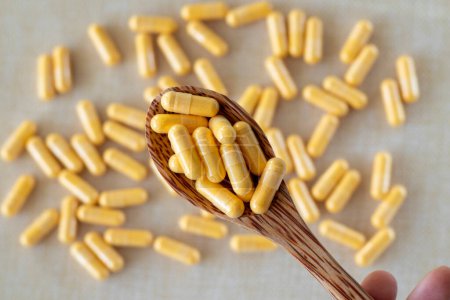 Photo for Lots of light yellow capsules in a wooden spoon on a white background. Supplements, vitamins, medications or pills - Royalty Free Image