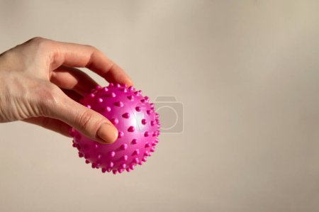 Photo for A woman is holding a pink ball with spikes. Myofascial release. Copy space, beige background - Royalty Free Image