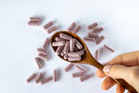 Foto de Cápsula rosa complementa las tabletas en una cuchara marrón sobre un fondo blanco, vista superior. Mujer con medicación, primer plano. - Imagen libre de derechos