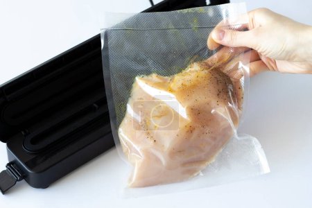 Téléchargez les photos : Morceau de poitrine de poulet sous vide mariné dans des épices à côté de la machine à emballer - en image libre de droit