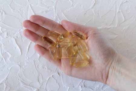 Photo for Large yellow capsules with Omega 3 or fish oil in a womans hand, close-up. Health and wellness, self-medication. - Royalty Free Image