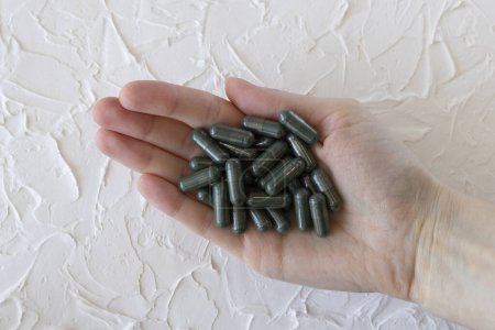 Foto de Medicamentos o suplementos verdes, clorofila o cápsulas de espirulina en una mano de mujer. - Imagen libre de derechos