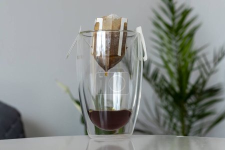 Der Prozess des Aufbrühens eines morgendlichen Kaffeetropfens mit einem Filterbeutel in einer durchsichtigen Tasse mit doppeltem Boden.