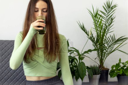 Eine schöne junge Frau mit einer schönen Figur trinkt den grünen Saft von Weizenkeimpflanzen
