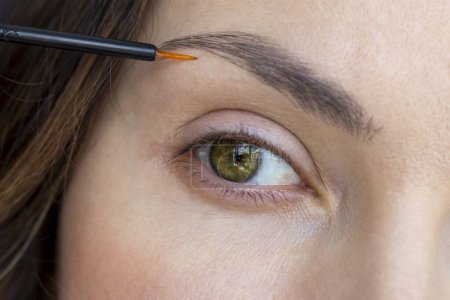 A woman applies eyebrow growth product, close-up.