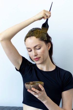 Téléchargez les photos : Belle femme teint ses cheveux avec un mélange à base de plantes de henné et de basma pour produire une couleur brune. - en image libre de droit