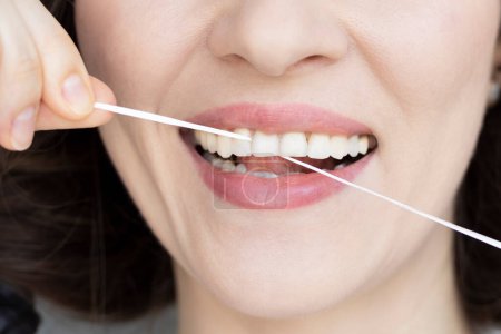 Woman brushing her teeth with dental tape close-up. Small distance between teeth.