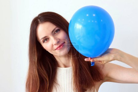 Mujer joven con un globo azul inflado sobre un fondo blanco.
