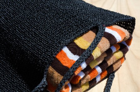 Foto de Bolso de rafia negro y toalla de colores sobre un fondo de madera. Bolso hecho a mano para mujer. - Imagen libre de derechos