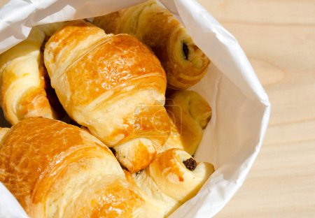 Téléchargez les photos : Croissant français fraîchement cuit dans une enveloppe en papier au soleil du matin. Délicieuses pâtisseries. - en image libre de droit