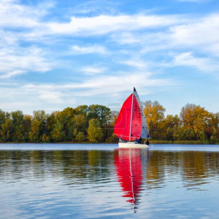Photo for A yacht with scarlet sails on the Dnieper River against the backdrop of an autumn landscape. Ukraine, Kyiv, Obolonsky district near a residential area, wild nature. - Royalty Free Image