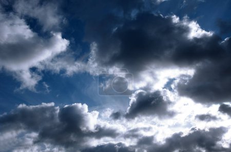 Bright light of the sun on a dark blue sky among the clouds. Dramatic view of the sun.