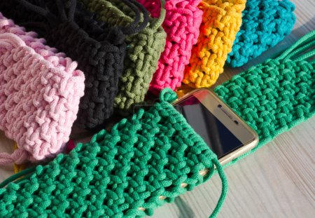 Kleine Handtasche für ein Handy. Strickmakram, Muster aus mehrfarbigen Baumwollschnüren. Handgemachtes Konzept, Hobby, Hintergrund, modischer Online-Strickkurs