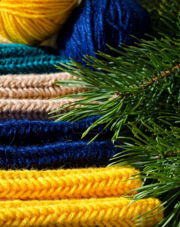 Mitones y tres bolas de hilo de lana sobre un fondo de un árbol de Navidad verde. Lana mezcla hilo para tejer ropa de abrigo para el invierno.