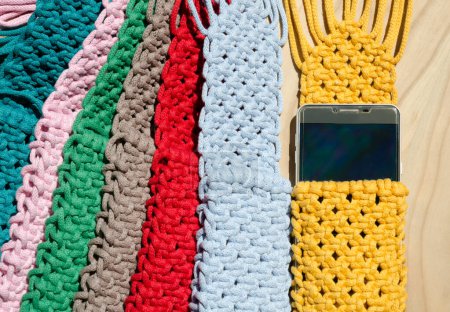 Small handbag for a mobile phone. Knitting macrame, pattern of multi-colored cotton cords. Handmade concept, hobby, background, fashionable online knitting course.