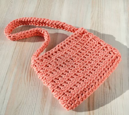 Small women's bag made of cotton cord. Fashionable peach fluff color bag on a light background.