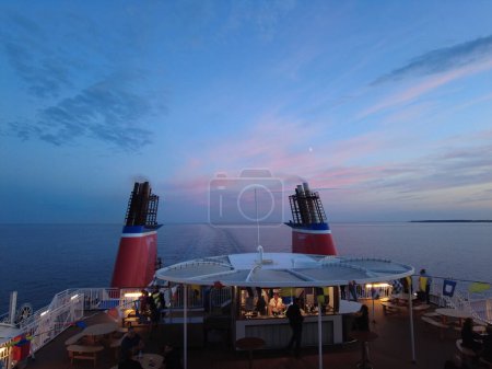 Photo for August 4, 2022 evening on baltic sea voyage, Stena Line ferry from Kiel Germany to Gothenburg Sweden, On the aft deck Stena Line ferry. People sit on terrace with drink on sun deck bar after sunset. - Royalty Free Image