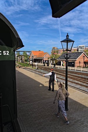 Photo for Departing train at the station, view on the perron with traditionally dressed conductor train guard track employee with signal sign in the Netherlands called Spiegelei, Hoorn, Netherlands 10-01-2023 - Royalty Free Image