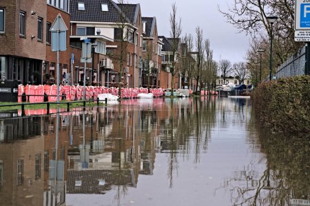 Téléchargez les photos : Le niveau élevé des eaux du lac provoque des inondations dans une rue de la ville néerlandaise après la tempête Henk. Les grands sacs et sacs de sable protègent les maisons et les immeubles contre les dégâts d'eau. Hoorn, Pays-Bas 01-05-2024. Photo horizontale - en image libre de droit
