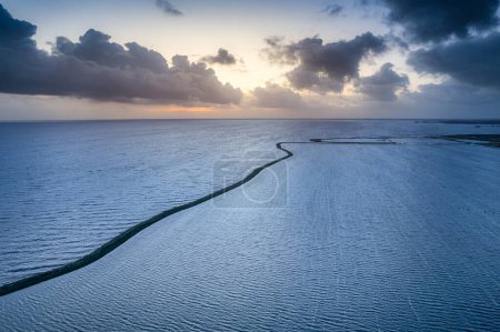 Aerial View of Winding Dike Path at Sunset by a Serene Lake in the Netherlands. Image captures the tranquil beauty of a winding dike separating two bodies of water as the sun sets on the horizon