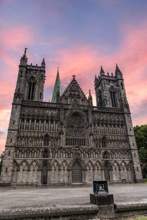 Sunset Over Nidaros Cathedral Facade With Statues in Trondheim Norway. The Nidaros Cathedral, with its detailed statues and Christ on a cross, stands against a vibrant evening sky