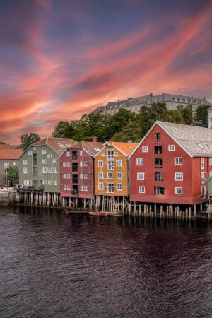 Colorful Brygge District Facades by nidelva river at Sunset in city Trondheim Norway. Vibrant, multi-colored houses on stilts along the river under a summer evening sky, tourist travel destination