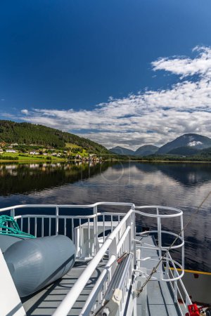 Fährdeck mit Blick auf das ruhige Wasser und die malerischen Berge rund um das Dorf Kvanne am Stangvikfjord, blauer Himmel mit weißen Wolken. Reiseziel in Norwegen