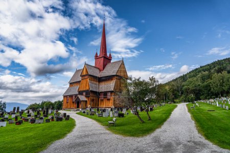 Vue sur l'église historique Ringebu Stave du XIIIe siècle se dresse au milieu de pierres tombales sous un ciel bleu avec des nuages en été, faisant écho à des siècles d'héritage norvégien.