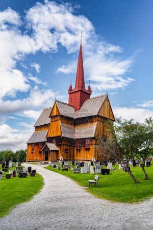 Vista de la histórica iglesia Ringebu Stave del siglo XIII se encuentra en medio de lápidas bajo un cielo azul con nubes en verano, haciendo eco de siglos de herencia noruega.