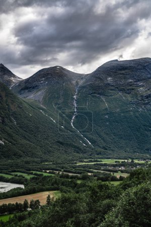 Towering Litlkalkinn mountain with a stream flowing down the mountainside towards the lush valley on a dark dramatic cloudy summer day near Sunndalsora in Norway