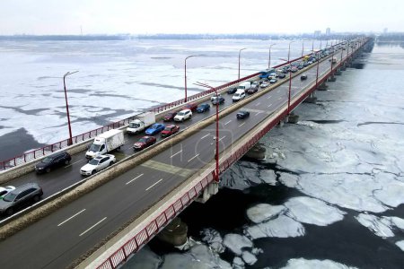 Photo for Many cars drive over river bridge in winter. Traffic jam, air pollution, smog on highway, road. Bridge in Dnipro Ukraine, aerial drone view - Royalty Free Image