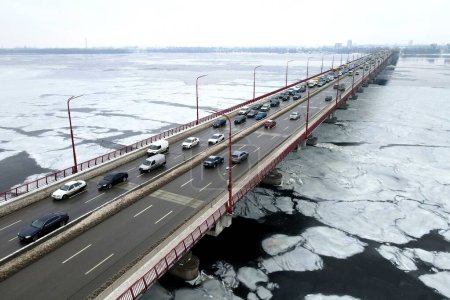 Foto de Muchos coches conducen por el puente del río en invierno. Atasco de tráfico, contaminación del aire, smog en la carretera, carretera. Puente en Dnipro Ucrania, vista aérea del dron - Imagen libre de derechos