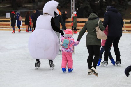 Photo for Ice rink in winter. Funny snowman teaches child to skate. Sports sections, active family sports, entertainment for children in the winter holidays - Royalty Free Image
