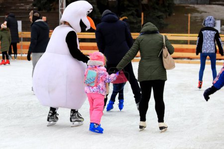Photo for Ice rink in winter. Funny snowman teaches child to skate. Sports sections, active family sports, entertainment for children in the winter holidays - Royalty Free Image